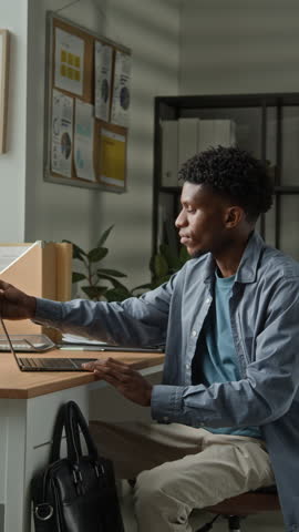 Vertical closeup of office worker putting laptop into black leather bag and preparing to leave modern office after workday in professional corporate environment