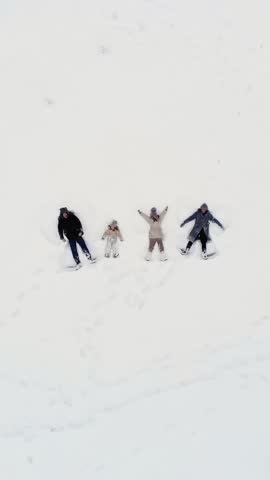 Winter family fun. Happy family of 4 are making angels on the snow. aero, top view. Family is enjoying of snow and snowfall, having fun on snowy winter day, outdoors.