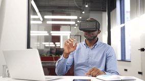 African american businessman works using VR glasses in virtual reality simulator sitting in business office. Black man worker uses gestures to control computer programs and flips through virtual pages - Powered by Shutterstock - Get 15% off with code: PIKWIZARD15