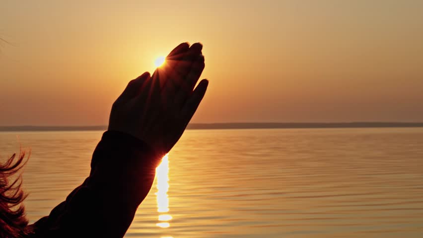 Woman praying at sunrise over calm water, hands together in worship and gratitude, perfect background for Christian praise, and the start of a new day.