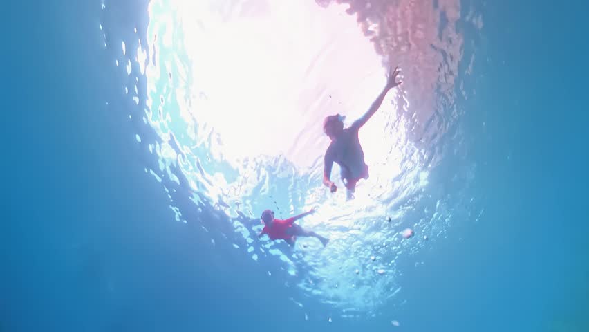 Two people swimming and snorkeling near the surface in clear tropical ocean water with sunlight filtering through, exploring the hidden underwater world of the coral reef. French Antilles in caribbean