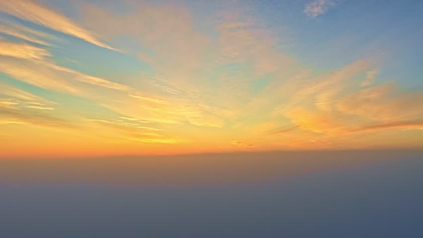 Drone rising shot showing bright circular sun sitting on dense indigo clouds with vibrant fiery orange and red horizon transitioning to golden yellow sky
