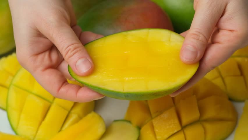 Hands showing and opening a fresh diced half of a mango fruit.