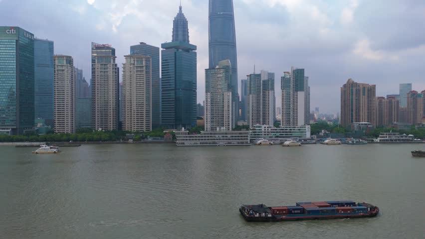 Aerial shot of the modern Shanghai skyline with numerous skyscrapers, corporate towers, and boats navigating the Huangpu River, Shanghai, China.