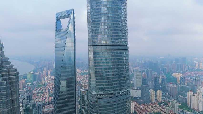 Aerial drone view of the Shanghai Tower and Shanghai World Financial Center skyscrapers dominating the dense, hazy urban skyline of Shanghai, China.