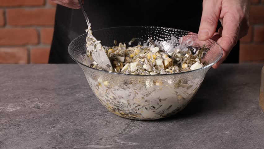 A cook mixes a salad with seaweed, egg and corn in a bowl.