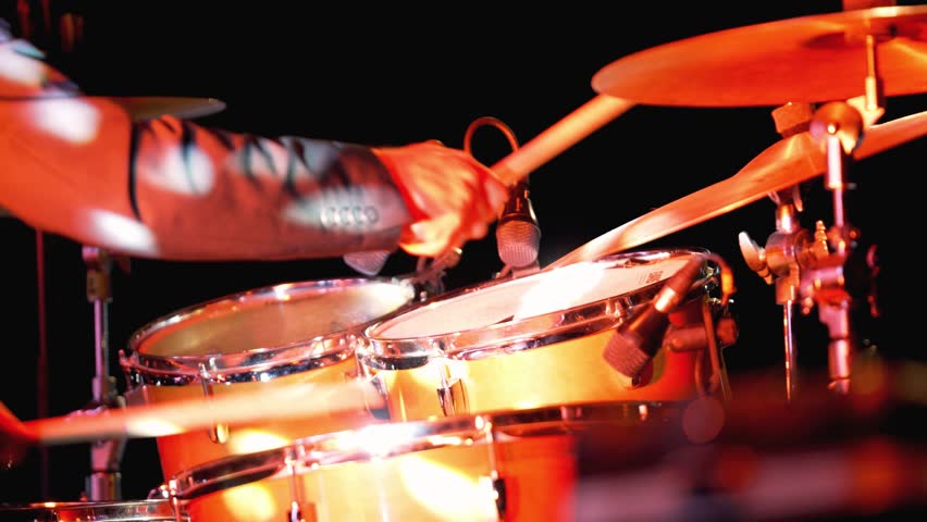 Drummer plays on stage at a live music event with bright lights and a focused audience. A drummer performs with energy in front of a lively crowd at a music event. Bright lights shine on the drums, creating an exciting atmosphere for all attendees.