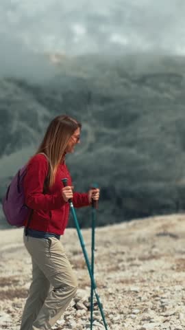 Fit female trekker with walking poles and a backpack hikes through a mountainous landscape. Dolomites, Italy.