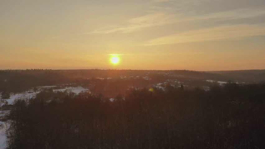 Sun rises in sky above snowy valley during winter trees hills are visible in distance, with homes peeking through landscape.