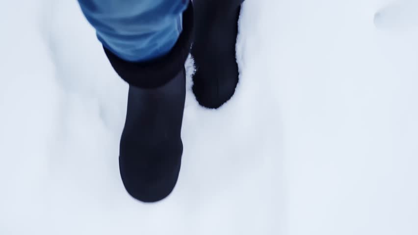 POV close-up of boots stepping through fresh snow, leaving footprints as someone walks along a cold winter path.