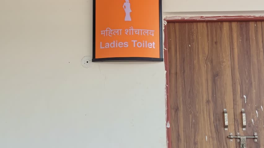 Tiltup shot of an orange ladies toilet signboard with Hindi and English text mounted on a station wall, clearly indicating women restroom facility inside premises