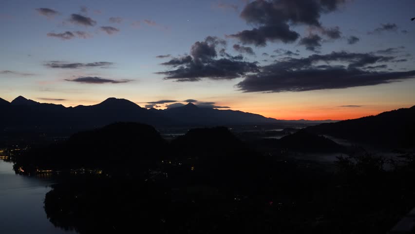 Morning aerial pan over Lake Bled as the sun rises, illuminating the lake and surrounding mountains.