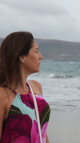 Beautiful thoughtful woman standing on the shore looking at the sea on a cloudy and windy day