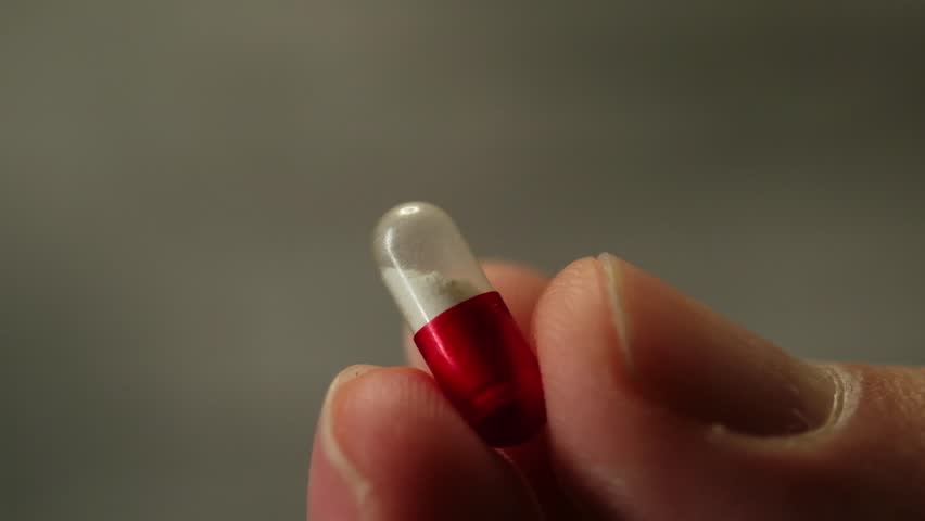 Slow motion close up video of a hand holding and rotating a red white antiviral pill, showing details to camera