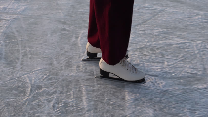 Close-up of woman ice skating on frozen lakewhite figure skates on frozen ice rink surface with scratch marks and patterns from skating blades