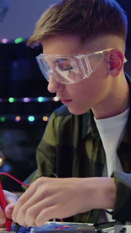Caucasian schoolboy in glasses with a tool repairs a home electronic appliance. Male professional boy repairs a computer. Engineer soldering microcircuit. Slow motion.