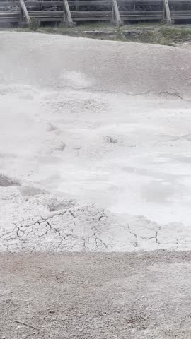 Bubbling geothermal mud pools at the Fountain Paint Pots in Yellowstone National Park. Thick mineral-rich mud churns and pops as steam rises from the surface, showcasing active geothermal activity in a natural volcanic landscape.