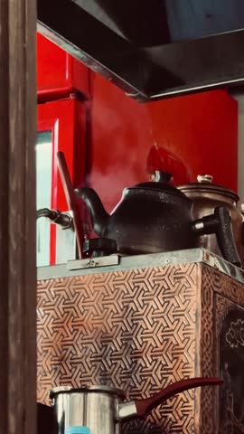 A black teapot with steam rising from it, sitting on a copper kettle.