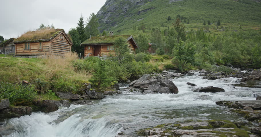 Traditional norwegian log cabins with green sod roofs by rushing river