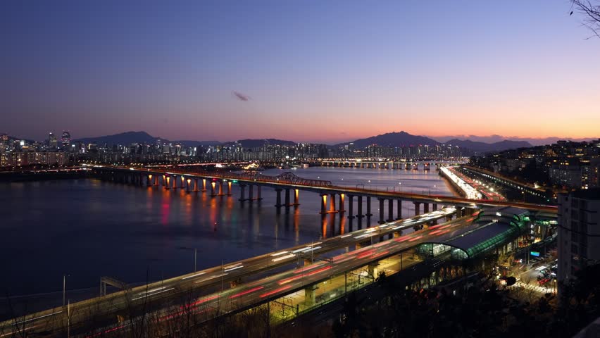 Long exposure blue hour to night transition time lapse showing Seoul city traffic light trails on Gangbyeonbuk-ro Expressway with Dongho Bridge and Oksu Station subway aerial view