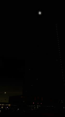 Total solar eclipse reaching totality over a city skyline at night. The sun