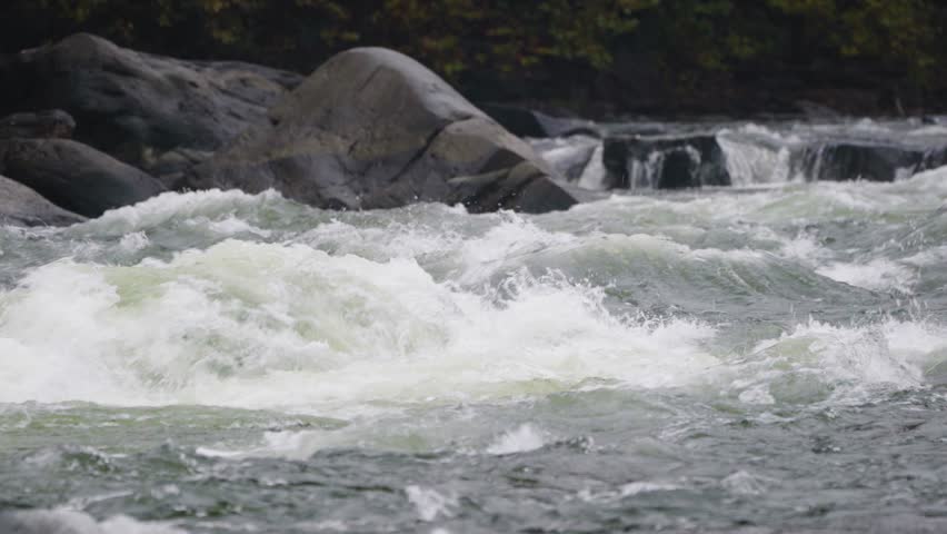 Raging whitewater rapids in mountain river with rocks background