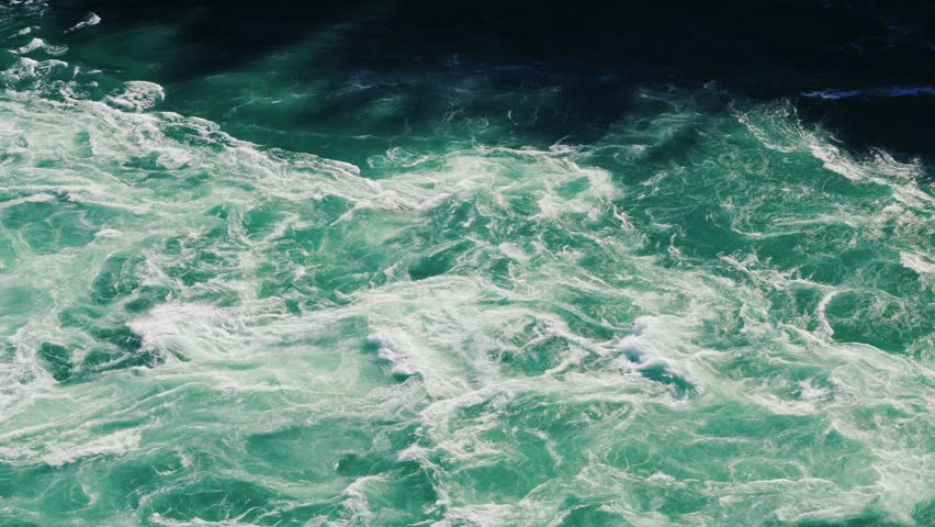 Churning turquoise water whirlpool in fast flowing river rapid with white foam and deep blue shadows