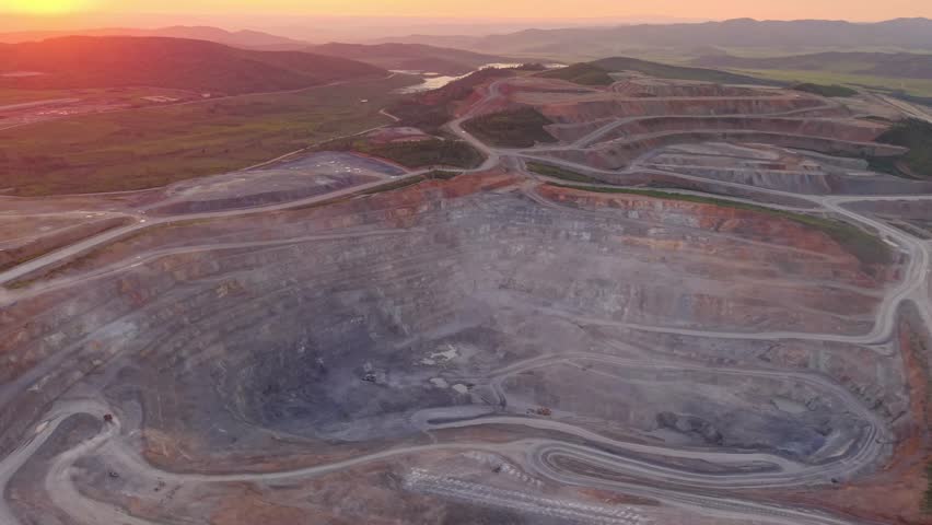 Aerial view of open pit mine at sunset with expansive landscape and dramatic sky, gold ore industry.