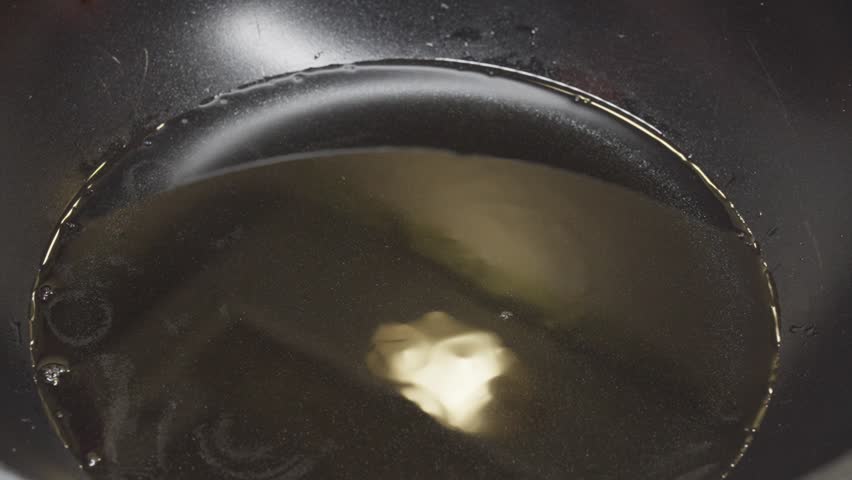 Close-up of stuffed chicken rolls placed in hot oil, beginning to cook in a pan.
