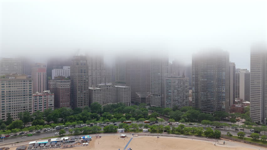 Chicago Illinois downtown seen from above with dense high rise buildings fading into fog, lakeshore park and beach below, muted daylight creating calm atmospheric urban scene.