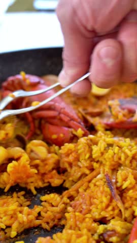 A person is eating food with a fork and spoon. The food is a mix of rice and meat