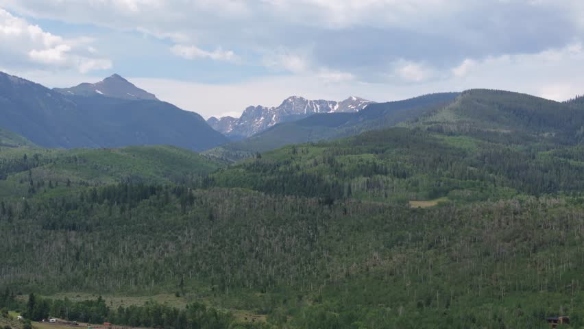 Vast mountain range with green forests and snow capped peaks under cloudy sky