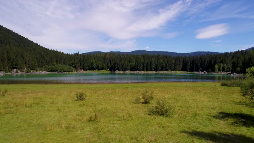 Aerial drone footage flying over calm lake with green forest background