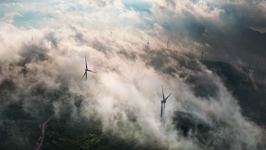 Aerial shot of many wind turbines on a misty mountain ridge generating green energy in the morning