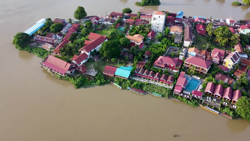 Drone footage following the Mekong River as it passes through Don Det town in the 4000 Islands region of Laos, with houses, boats, and riverside vegetation.