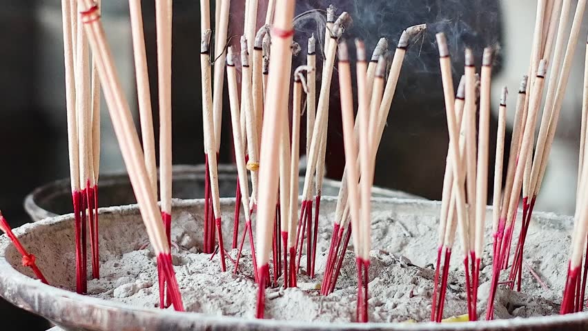 A detailed close-up shot of numerous incense sticks burning and smoldering in a ceramic pot.