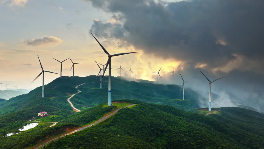 Wind turbine farm on green mountain with winding road scenery at sunset 