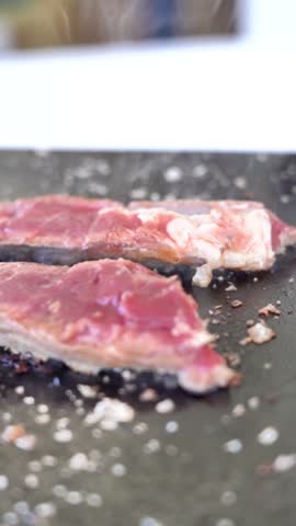 A piece of meat is being cooked on a grill. The meat is brown and has a lot of seasoning on it