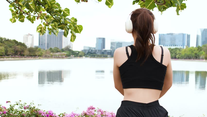A young woman in fitness gear stretches her legs beside a lake with city skyline