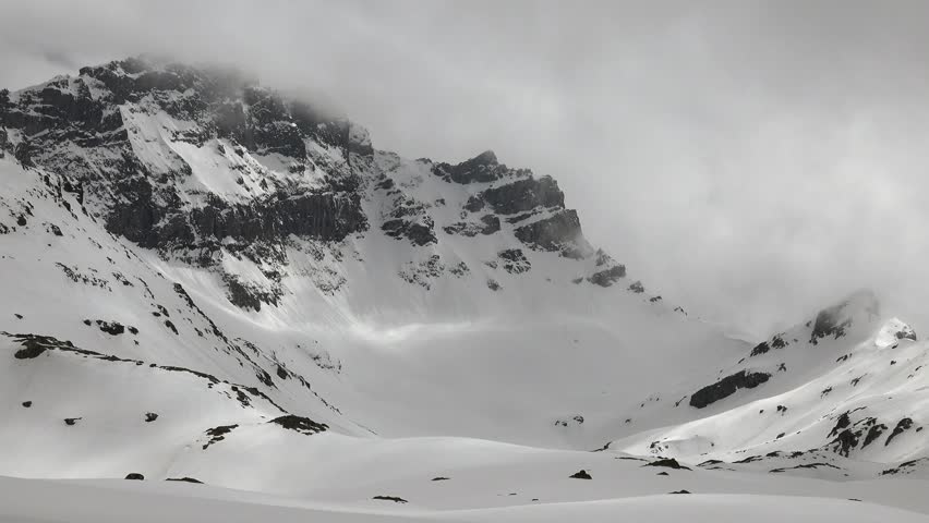 Snow covered Caucasus mountain peaks rise above vast alpine valleys under dramatic winter skies. Rugged ridges and icy slopes define the remote highland landscape.