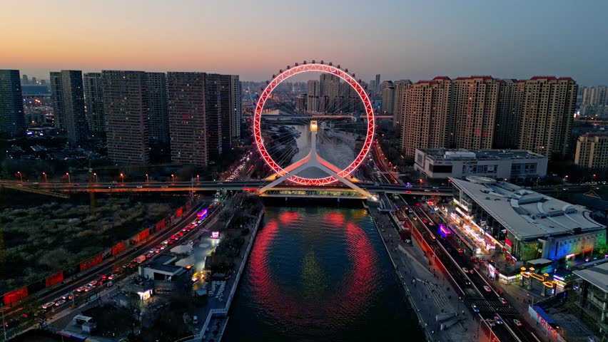 Aerial view of the radiant red Tianjin Eye Ferris wheel reflecting in the river, juxtaposed against the city
