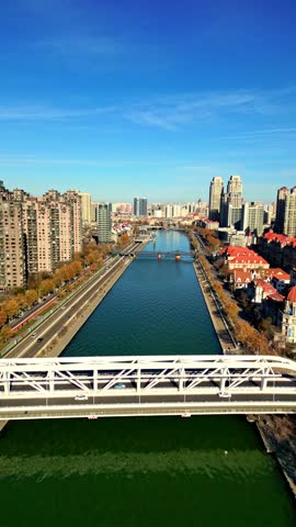 Aerial view of the Hai River flowing through the city, reflecting the clear blue sky amidst tall buildings, Tianjin, Tianjin, China.