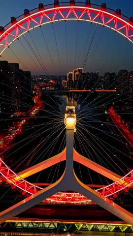 Aerial view of the illuminated Tianjin Eye Ferris wheel against the dark sky, a beacon of light in the city, Tianjin, Tianjin, China.