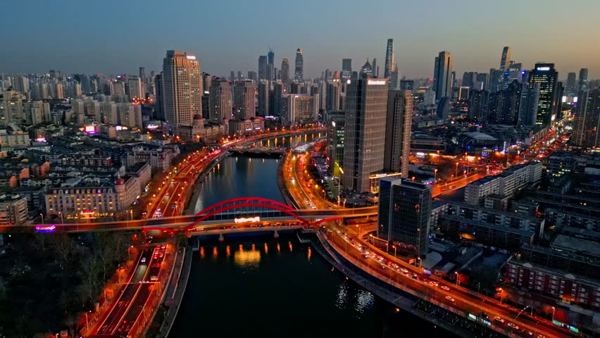 Aerial view of the bustling Tianjin cityscape, a symphony of glowing lights reflecting on the river at dusk, Tianjin, Tianjin, China.