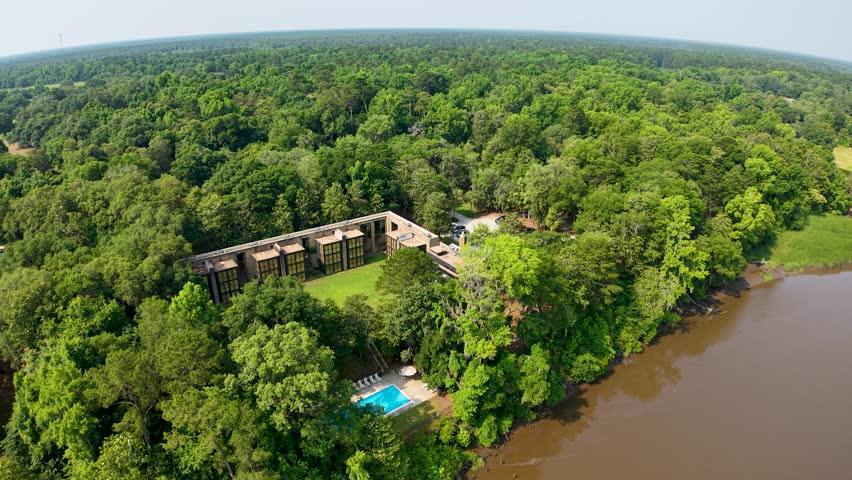 Drone footage shows an old stone ruin with a blue pool beside a broad river surrounded by lush green forest and marshland at Middleton Place Plantation in South Carolina, capturing both historic archi