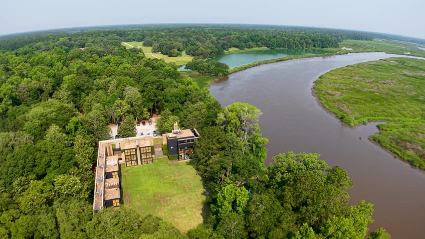 Drone footage captures an aerial view of an old stone building or ruins situated beside a winding river and lush green marshland at Middleton Place Plantation in South Carolina, highlighting the blend