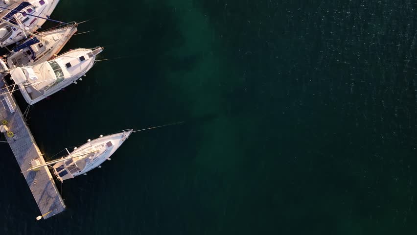 Aerial view of boats docked in a harbour, contrasting the white boats against the dark green water, creating a serene scene, Sardinia, Italy.