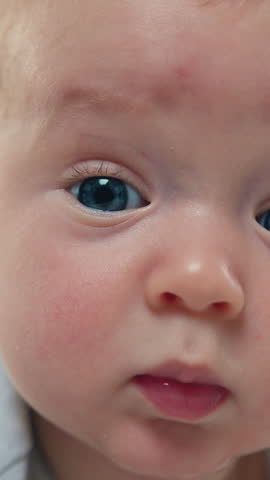 Close up of pretty newborn baby boy lying in cot on his stomach and joyful looking at camera. Adorable three-month-old toddler lying on stomach in his crib and posing, looking at camera at home