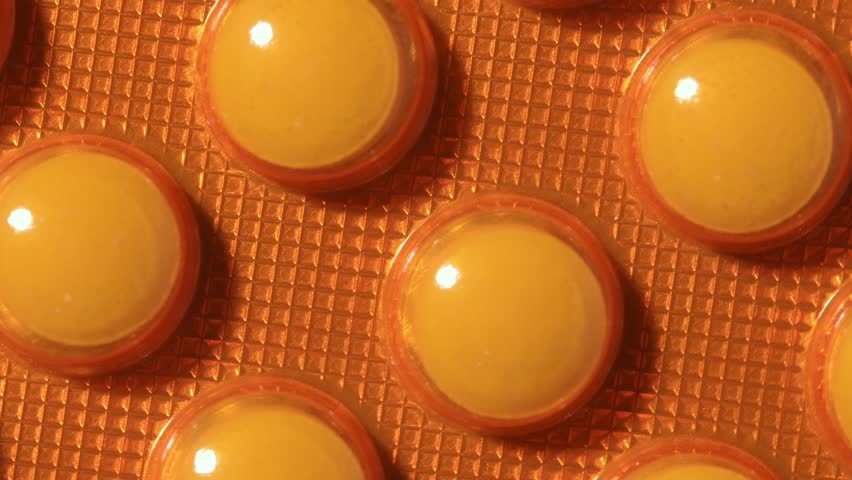 Rotation reveals orange blister pack with round tablets, textured close-up for pharmacy, dosage control, medication safety.