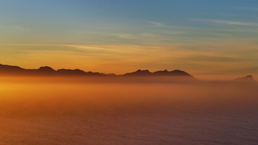 Aerial view of the rugged mountain range shrouded in a thick fog, with the ocean visible in the foreground, Cape Town, Western Cape, South Africa.